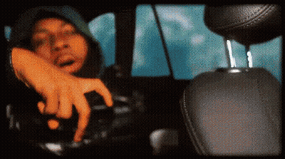 A Man In A Hooded Jacket Is Driving A Car GIF