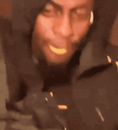 A Man In A Hooded Jacket Is Eating A Piece Of Food . GIF