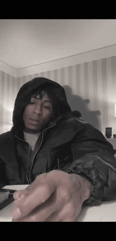 A Man In A Hooded Jacket Is Sitting At A Table In A Room With A Striped Wall . GIF