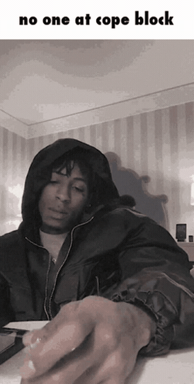A Man In A Hooded Jacket Is Sitting At A Table With The Words No One At Cope Block Above Him GIF
