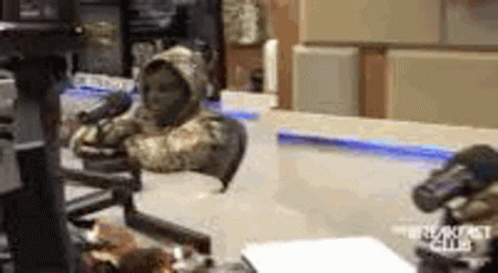 A Man In A Hooded Jacket Is Sitting In Front Of A Microphone In A Room . GIF