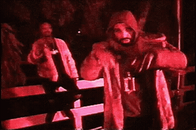 A Man In A Hooded Jacket Is Standing In A Dark Room Holding A Bag . GIF