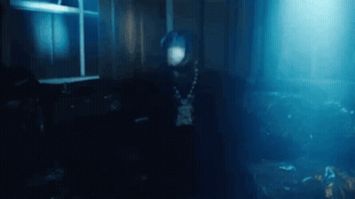 A Man In A Hooded Jacket Is Standing In A Dark Room . GIF