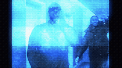 A Man In A Hooded Jacket Is Standing In A Dark Room GIF