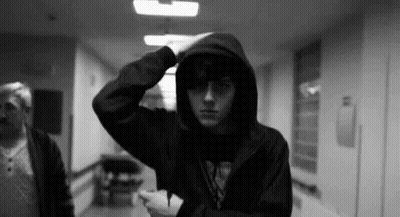 A Man In A Hooded Jacket Is Standing In A Hallway . GIF