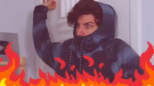 A Man In A Hooded Jacket Is Standing In Front Of A Door With Flames Behind Him GIF