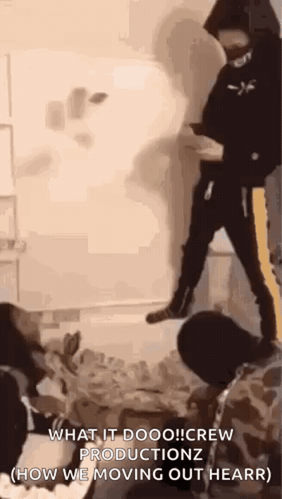 A Man In A Hooded Jacket Is Standing On A Pile Of Bottles In A Room . GIF