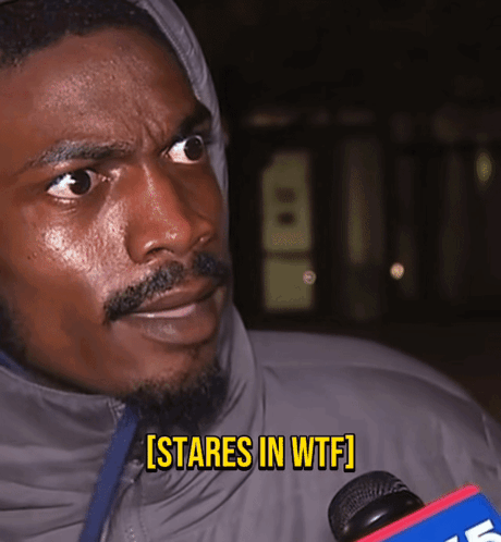 A Man In A Hooded Jacket Says [ Stares In Wtf ] While Holding A Microphone GIF