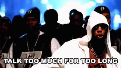 A Man In A Hooded Jacket Stands In Front Of A Crowd With The Words " Talk Too Much For Too Long " Below Him GIF