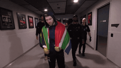 A Man In A Hooded Jacket With The Word Ufc On It Is Walking Down A Hallway GIF