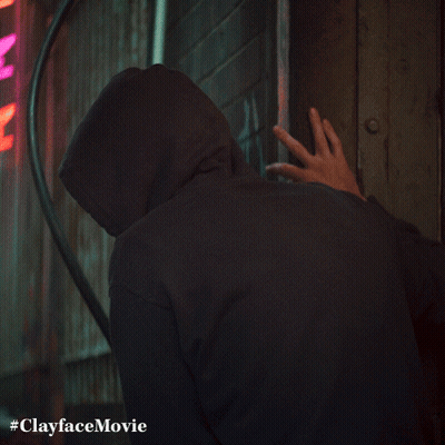 A Man In A Hooded Sweatshirt Is Standing In Front Of A Neon Sign That Says Clayface Movie GIF