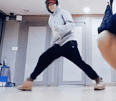 A Man In A Hoodie Is Dancing In A Room With A Woman Standing Behind Him . GIF