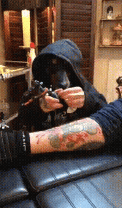 A Man In A Hoodie Is Getting A Tattoo On Another Man 'S Arm GIF