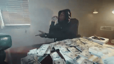 A Man In A Hoodie Is Sitting At A Table With A Pile Of Money On It . GIF