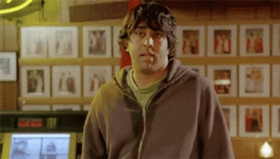 A Man In A Hoodie Is Smoking A Cigarette In Front Of A Wall Of Pictures . GIF