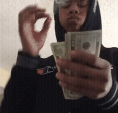 A Man In A Hoodie Is Smoking A Cigarette While Holding A Bunch Of Money . GIF