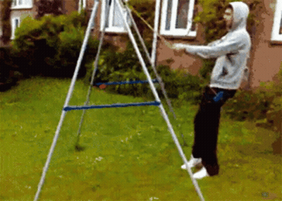 A Man In A Hoodie Is Standing In Front Of A Swing Set In A Yard GIF