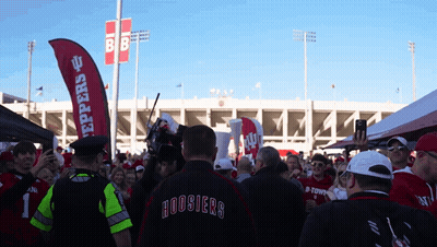 A Man In A Hoosier 'S Jacket Stands In Front Of A Crowd GIF