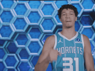 A Man In A Hornets Jersey Stands In Front Of A Honeycomb Pattern GIF