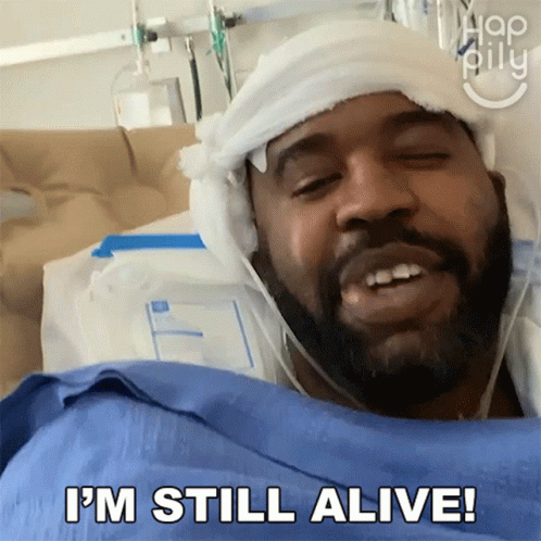 A Man In A Hospital Bed With A Bandage On His Head Says " I 'M Still Alive " GIF