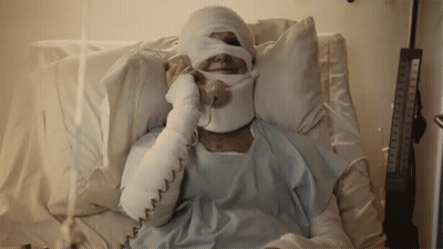 A Man In A Hospital Bed With A Bandaged Head Talking On A Phone GIF