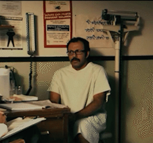 Man In Hospital Gown Sitting At Desk With Malaria Poster GIF