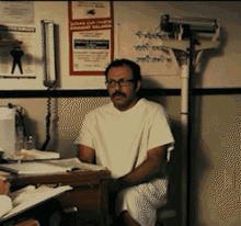 Man In Hospital Gown Sitting At Desk With Ambulance Sign GIF