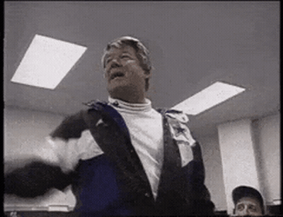 A Man In A Jacket Is Standing In A Room With A Man In A Baseball Cap . GIF
