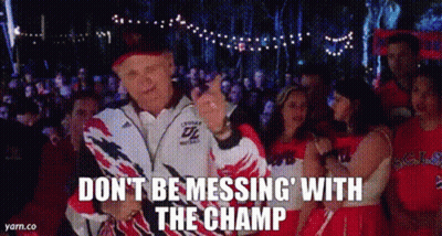 A Man In A Jacket Is Standing In Front Of A Crowd Of People And A Cheerleader . GIF