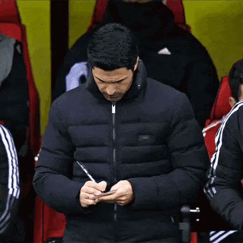 A Man In A Jacket Is Writing On A Piece Of Paper With A Pen . GIF