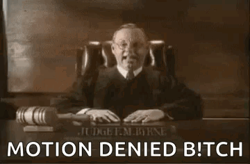 A Man In A Judge 'S Robe Is Sitting At A Desk With A Microphone And A Hammer . GIF