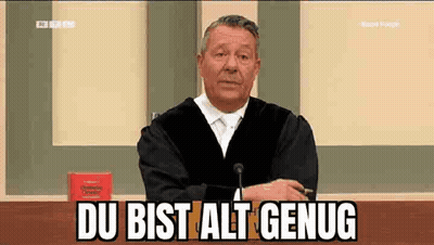 A Man In A Judge 'S Robe Is Sitting At A Table In Front Of A Microphone And Says Du Bist Alt Genug GIF