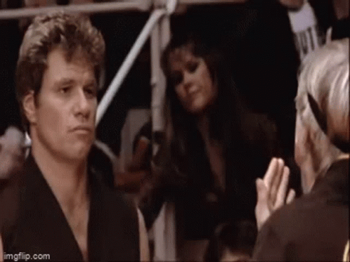 A Man In A Karate Uniform Is Standing In A Crowd Of People . GIF