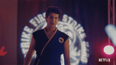 A Man In A Karate Uniform Is Standing In Front Of A Sign That Says Strike Fire Strike . GIF