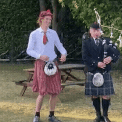 A Man In A Kilt Is Playing A Bagpipe Next To Another Man In A Kilt GIF