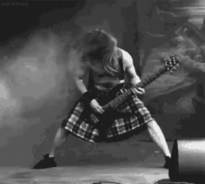 A Man In A Kilt Is Playing A Guitar On Stage In A Black And White Photo . GIF