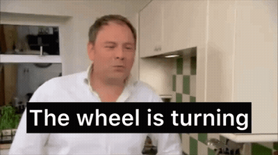 A Man In A Kitchen With The Words `` The Wheel Is Turning '' Behind Him . GIF