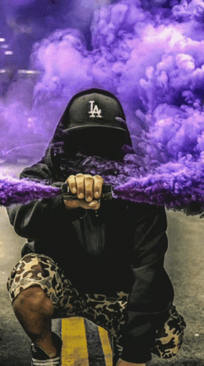 A Man In A La Hat Holds A Purple Smoke Bomb GIF