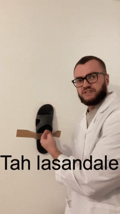 A Man In A Lab Coat Is Holding A Pair Of Sandals In Front Of A Wall That Says Tah Lasantale GIF