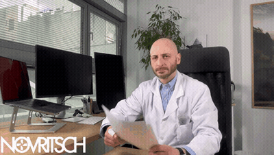 A Man In A Lab Coat Is Sitting At A Desk With The Word Novritsch On The Bottom Right GIF