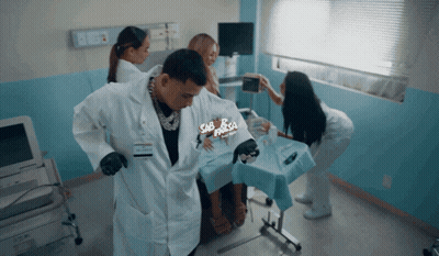 A Man In A Lab Coat Is Standing Next To A Woman In A Hospital Bed With A Sign That Says Sabrosa GIF