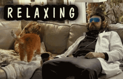 A Man In A Lab Coat Sits On A Couch With A Cat And A Sign That Says Relaxing GIF