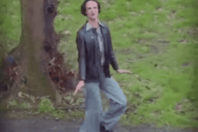 A Man In A Leather Jacket And Blue Jeans Is Dancing In The Woods . GIF