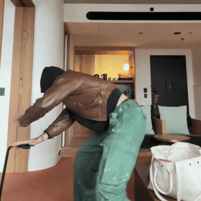 A Man In A Leather Jacket And Green Pants Is Standing In A Room GIF