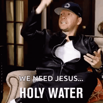 A Man In A Leather Jacket And Hat Is Sitting On A Couch And Saying We Need Jesus ... Holy Water . GIF