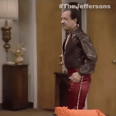 A Man In A Leather Jacket And Red Pants Is Standing In A Room . GIF