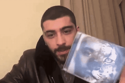 A Man In A Leather Jacket Is Holding A Cd With A Picture Of A Lion On It . GIF