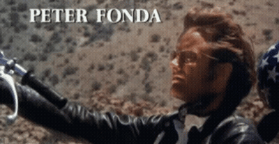A Man In A Leather Jacket Is Holding A Motorcycle Handlebars And The Name Peter Fonda Is Visible Above Him GIF