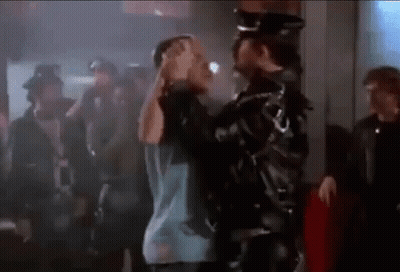 A Man In A Leather Jacket Is Holding Another Man 'S Head In A Crowd Of People . GIF