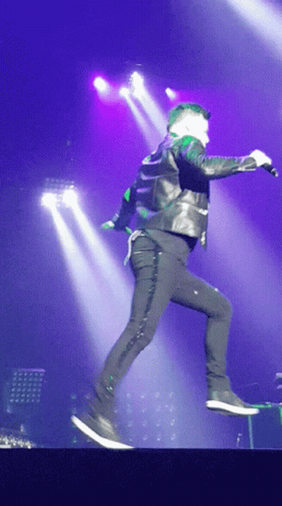 A Man In A Leather Jacket Is Jumping In The Air With A Microphone GIF